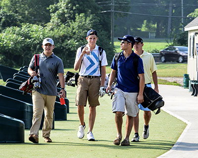 Four guys walking near golf course with golfing clothes and equipment